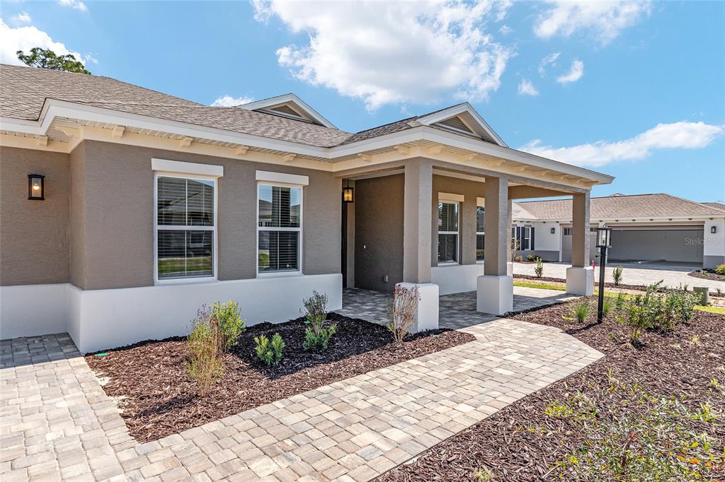 A tan house with a covered entryway, stone walkway, and a detached garage in the background — 10815 SW 96TH LANE ROAD, OCALA, FL