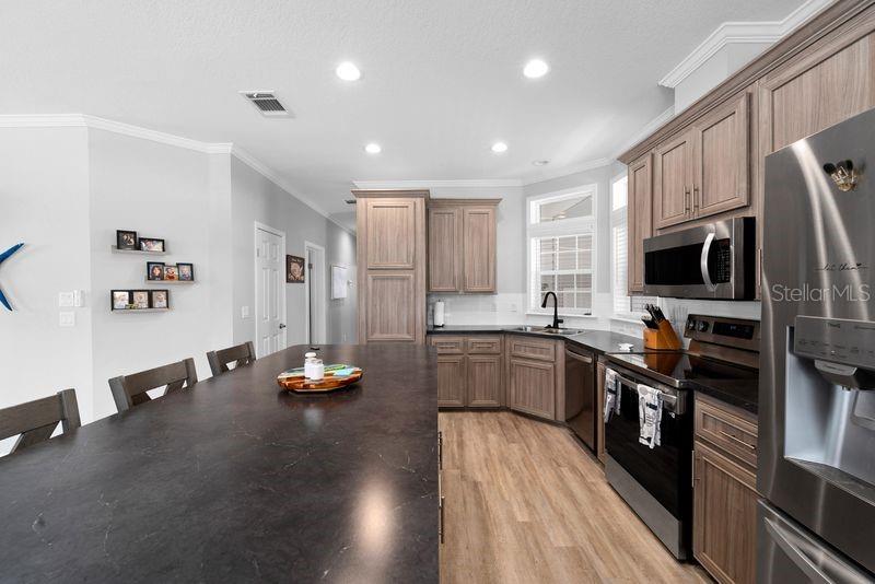 A kitchen features dark countertops, light wood cabinetry, stainless steel appliances, and light wood flooring — 8903 SHELDON WEST DRIVE, TAMPA, FL