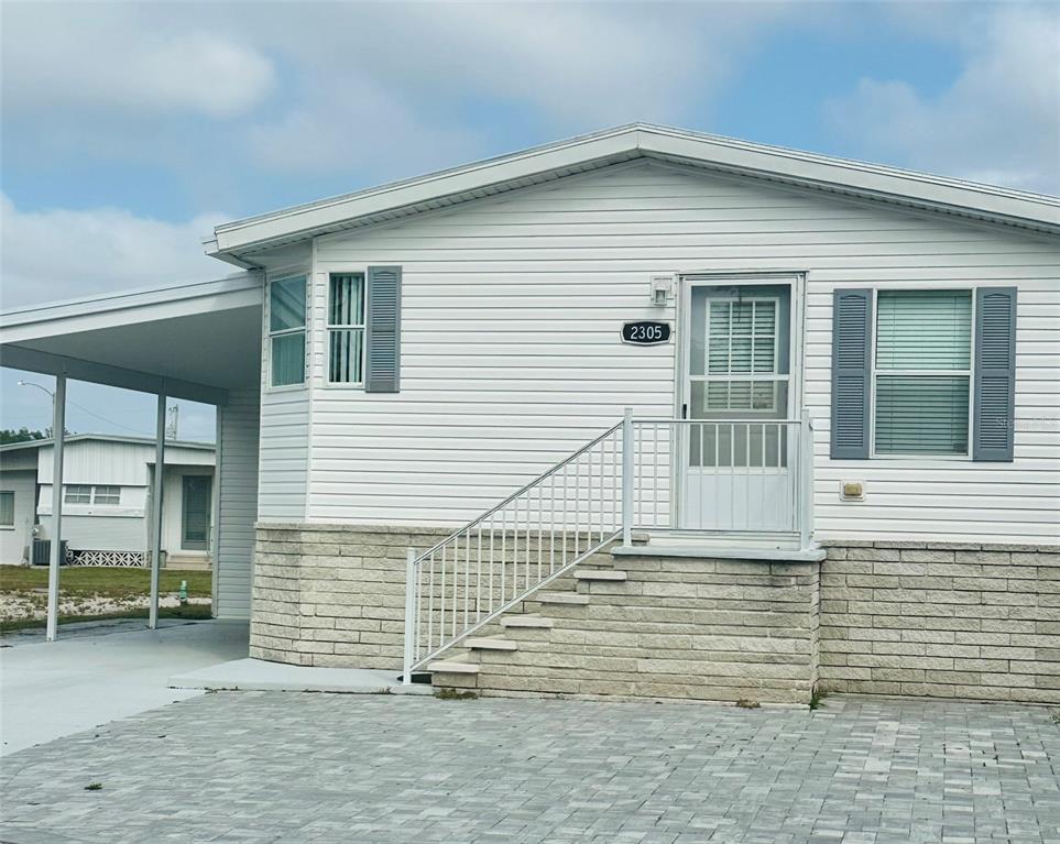 A white mobile home features a stone-patterned base, a carport, and a front staircase — 2305 BAY DRIVE, BRADENTON, FL