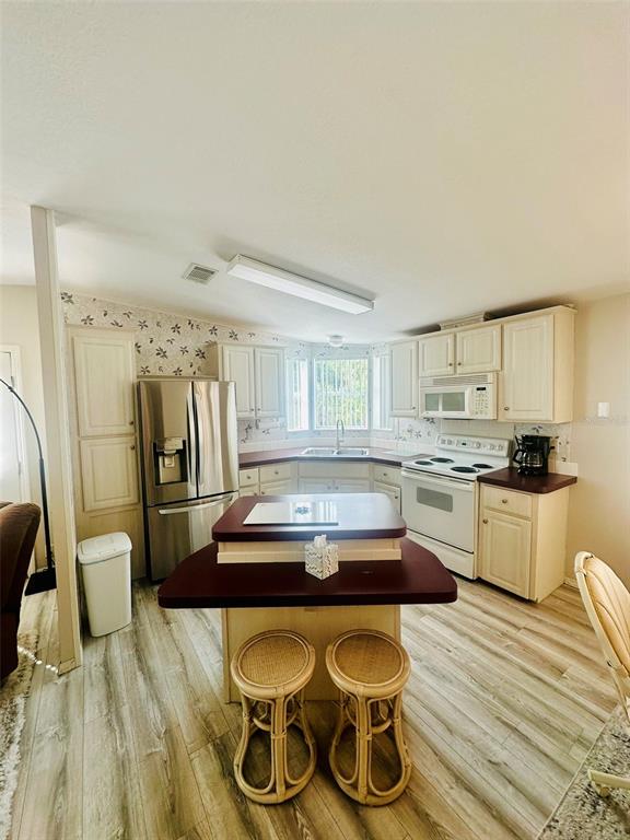 A kitchen features white cabinets, stainless steel appliances, a central island, and wood-look flooring — 2305 BAY DRIVE, BRADENTON, FL