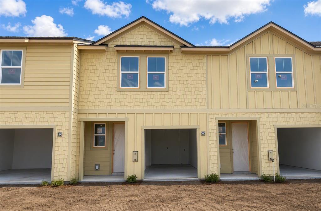 The exterior of a multi-unit townhouse complex features yellow siding, shingle accents, and open garages — 7538 DEER VALLEY CIRCLE, TAMPA, FL