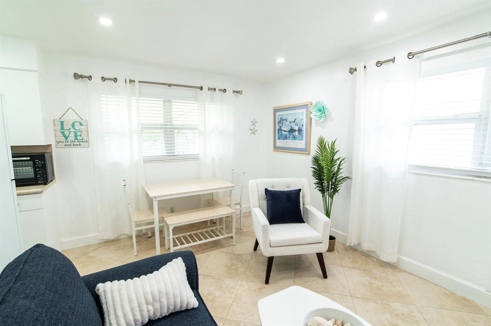 A bright living and dining area features white walls, tile flooring, and a white armchair — 3230 NE 13th Street # 203, Pompano Beach FL 33062, POMPANO BEACH, FL