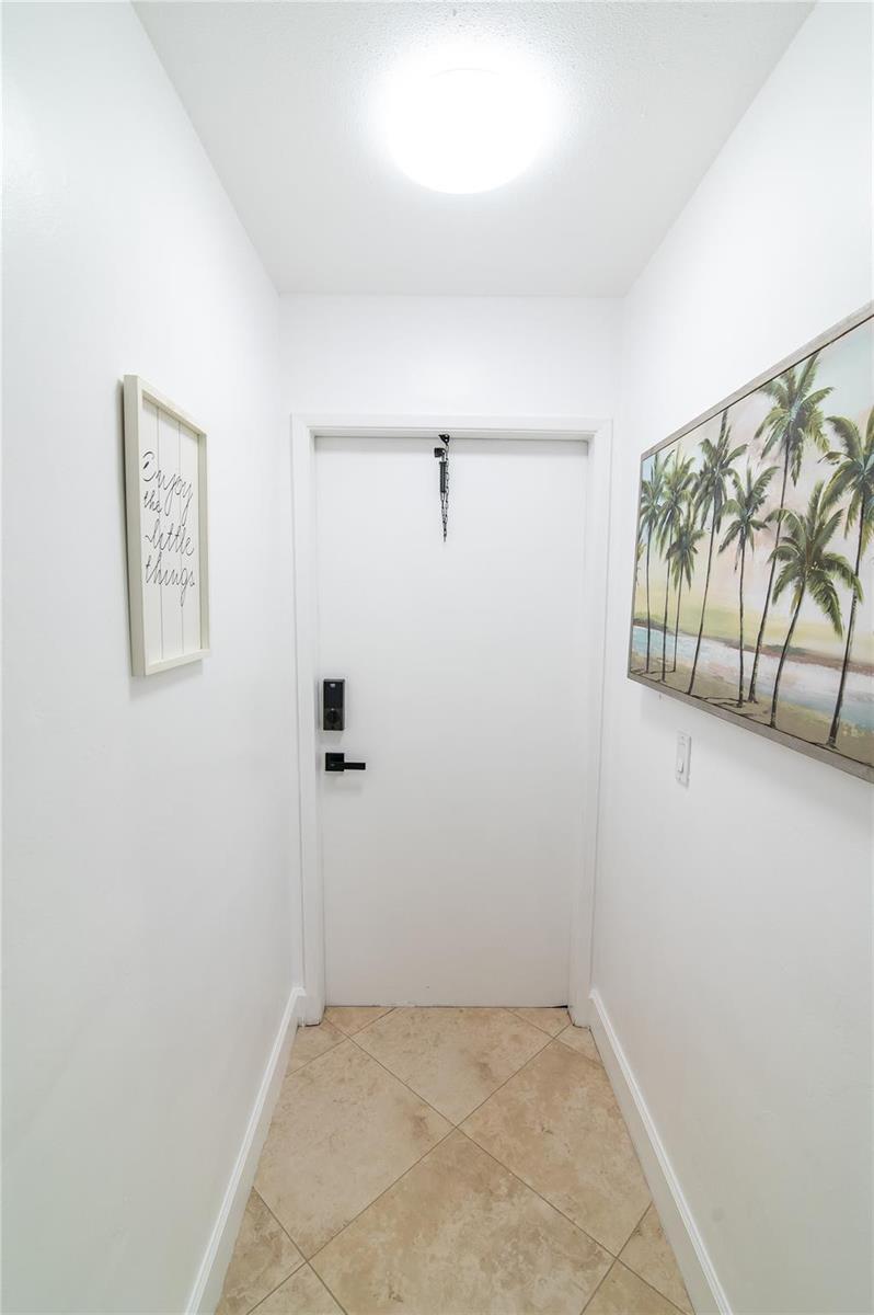 A narrow entryway features white walls, tile flooring, a white door, and wall art — 3230 NE 13th Street # 203, Pompano Beach FL 33062, POMPANO BEACH, FL