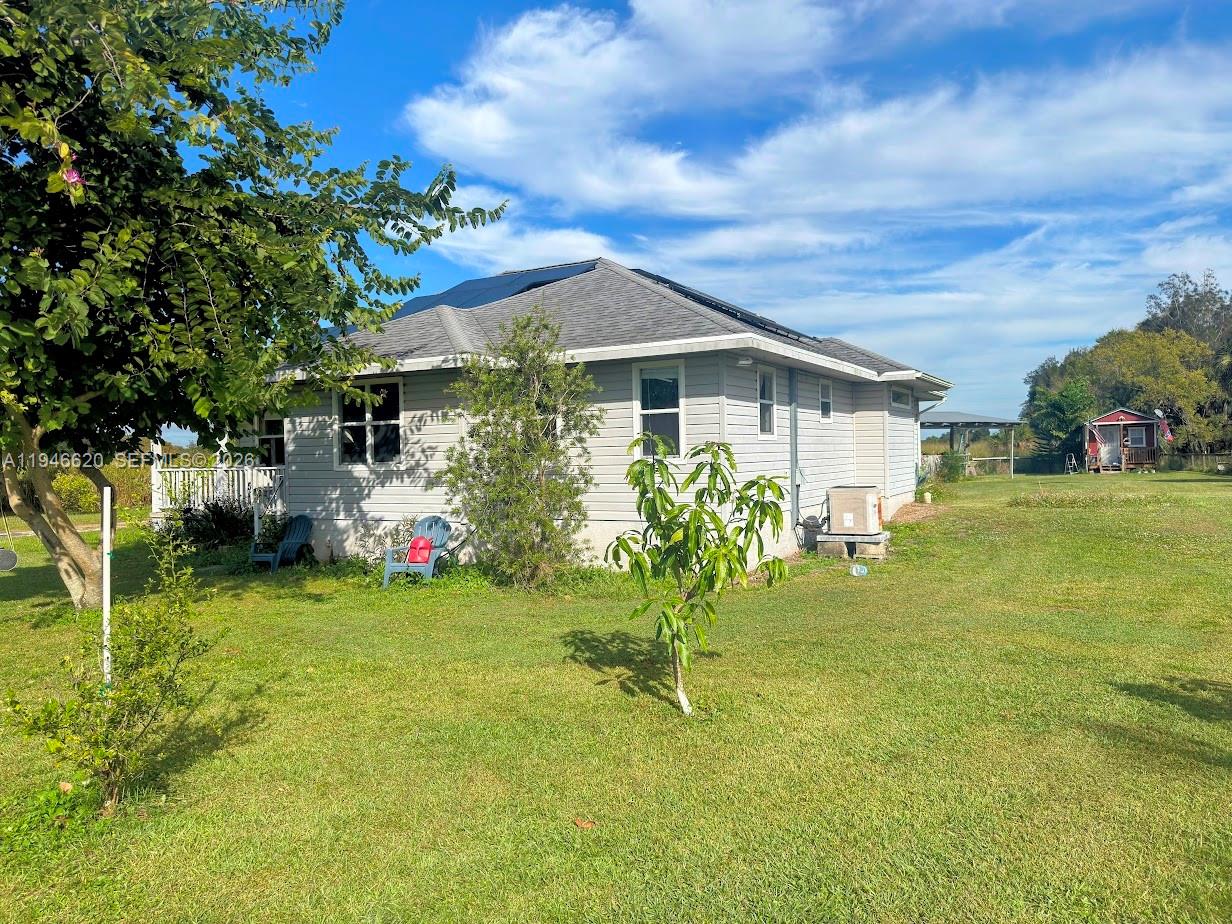 A covered porch features a ceiling fan, white railings, and two folding chairs overlooking a yard — 2915 Ortona Locks Rd, Moore Haven FL 33471, MOORE HAVEN, FL