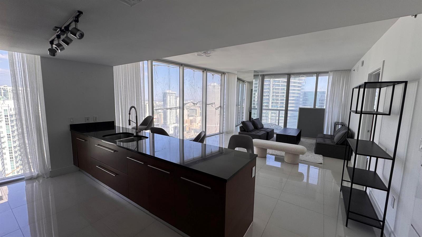 A modern kitchen island with dark cabinetry faces a living area with floor-to-ceiling windows — 475 Brickell Avenue # 4615, Miami FL 33131, MIAMI, FL