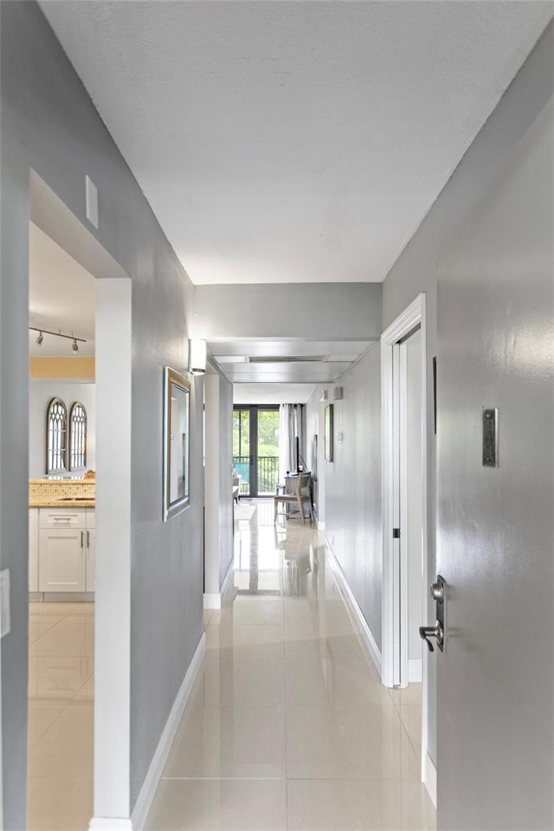 A hallway with light-colored tile flooring leads toward a living area with a balcony view — 16 Royal Palm Way # 302, Boca Raton FL 33432, BOCA RATON, FL