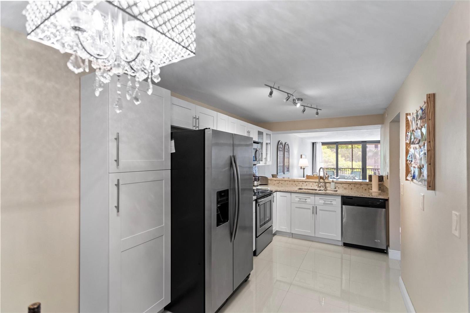 A kitchen with white cabinets, stainless steel appliances, tile flooring, and a crystal chandelier — 16 Royal Palm Way # 302, Boca Raton FL 33432, BOCA RATON, FL