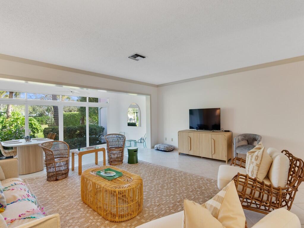 A living room with wicker furniture, a television console, and large windows overlooking a garden — VERO BEACH, FL