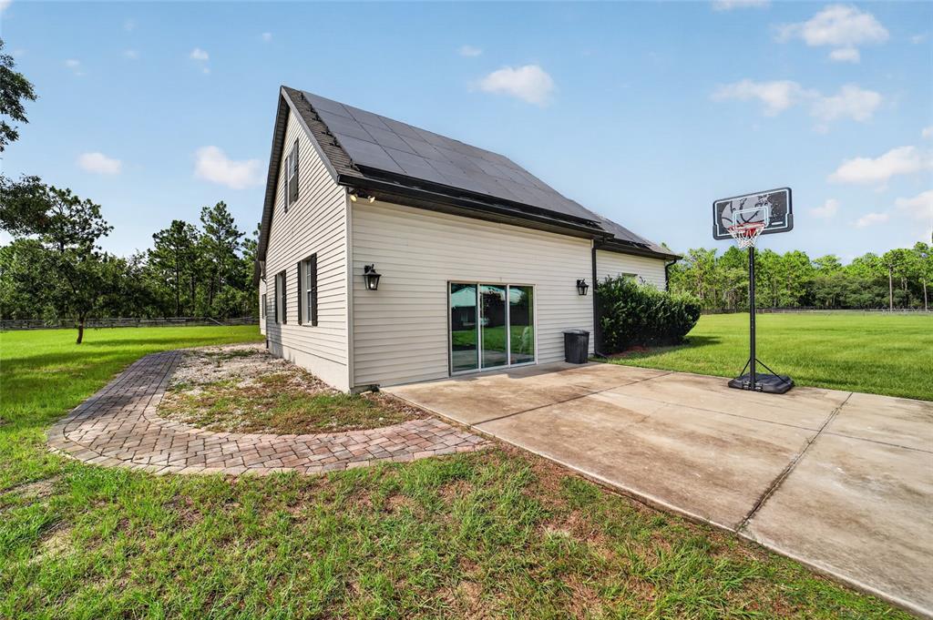 A beige house with solar panels on the roof, a concrete patio, and a basketball hoop — 6351 SE 140 AVENUE, MORRISTON, FL