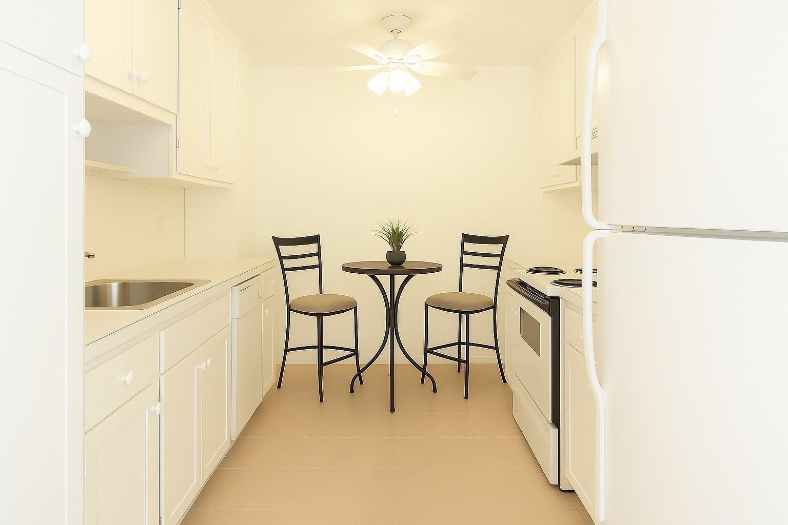 A galley kitchen with white cabinets, white appliances, and a small bistro table for two — 4001 Hillcrest Drive # 407, Hollywood FL 33021, HOLLYWOOD, FL