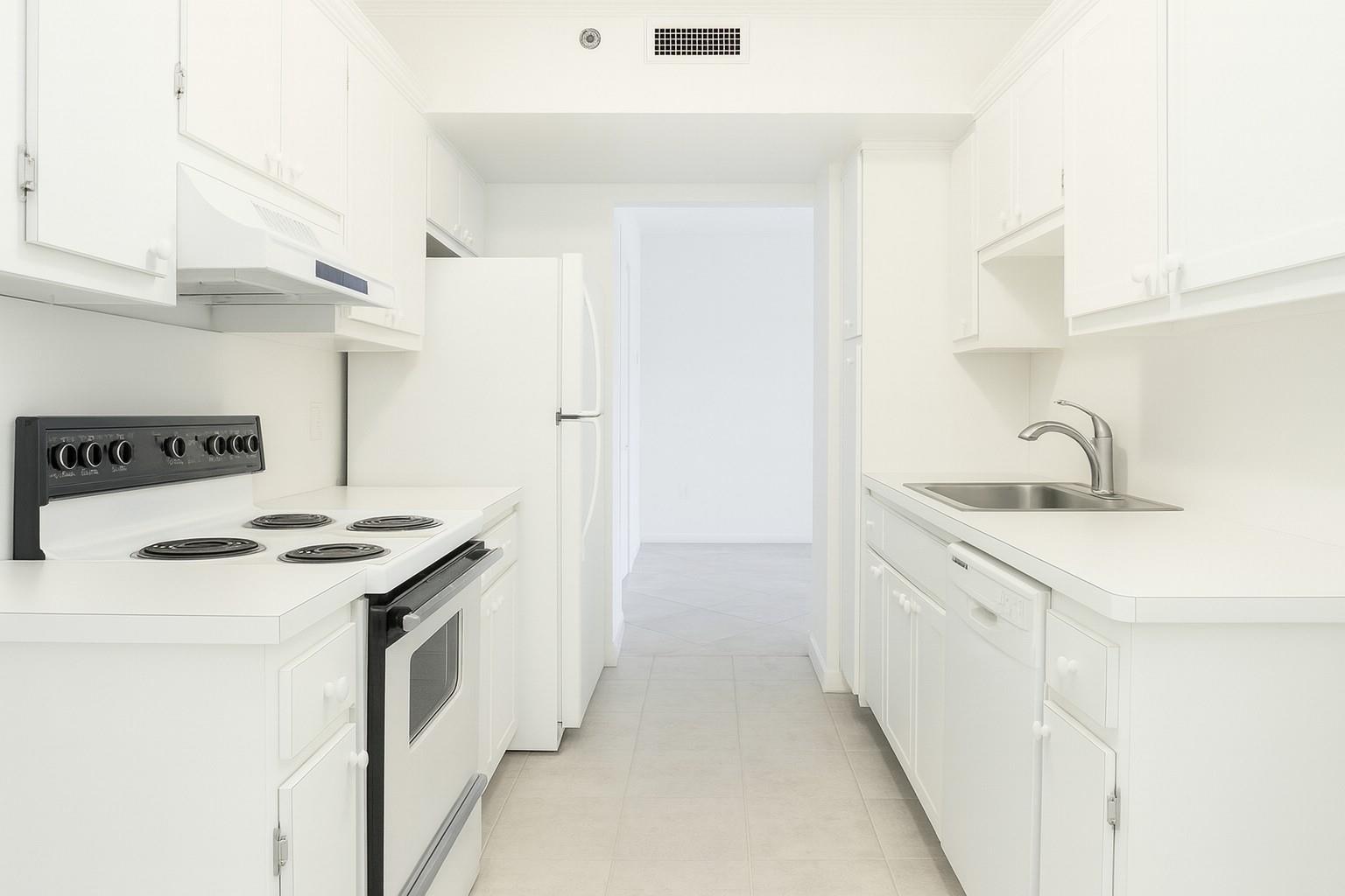 A galley-style kitchen features white cabinets, white appliances, and light-colored tile flooring — 4001 Hillcrest Drive # 407, Hollywood FL 33021, HOLLYWOOD, FL