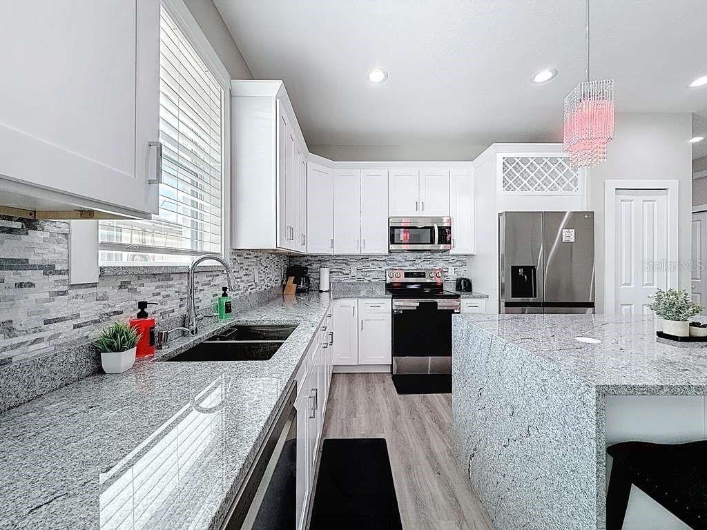 A kitchen features white cabinets, granite countertops, a tiled backsplash, and a central island — 1409 W WOOD STREET, TAMPA, FL