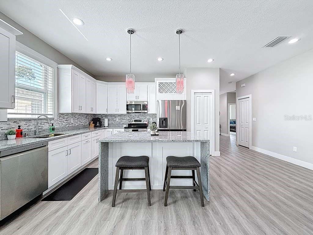 A modern kitchen features white cabinetry, granite countertops, a central island, and stainless steel appliances — 1409 W WOOD STREET, TAMPA, FL