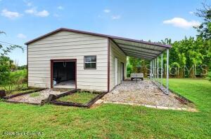A metal workshop building with an attached carport sits on a gravel lot — 1475 DALBORA ROAD, MERRITT ISLAND, FL