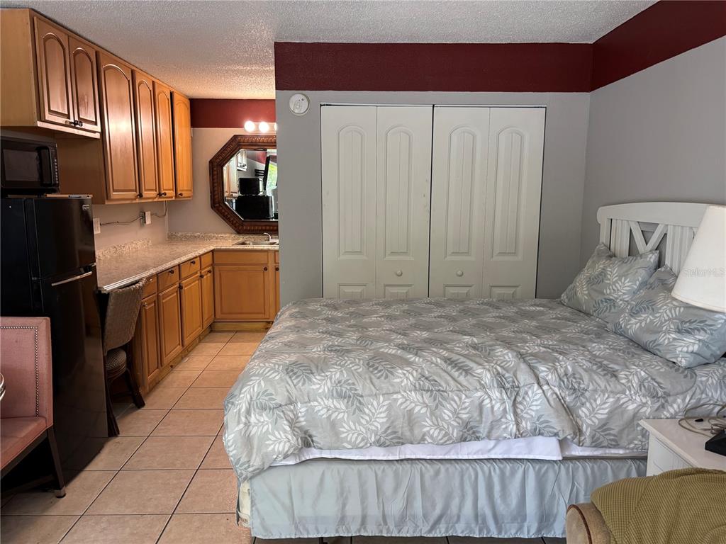A bedroom features a kitchenette with wooden cabinets, a bed, and white closet doors — 7900 S ORANGE BLOSSOM TRAIL UNIT 2009, ORLANDO, FL