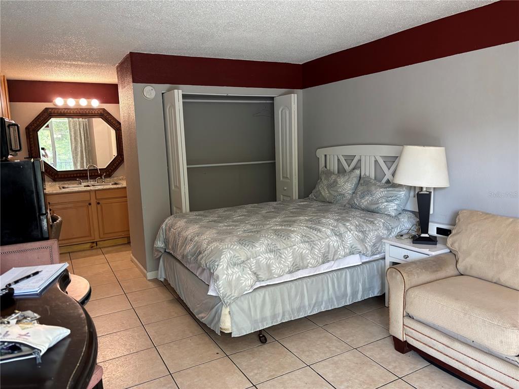 A bedroom features a bed, a closet, a vanity area, and a sofa on tile flooring — 7900 S ORANGE BLOSSOM TRAIL UNIT 2009, ORLANDO, FL