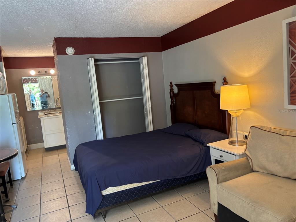 A bedroom with a bed, closet, and small kitchenette area with tiled flooring — 7900 S ORANGE BLOSSOM TRAIL UNIT 2009, ORLANDO, FL