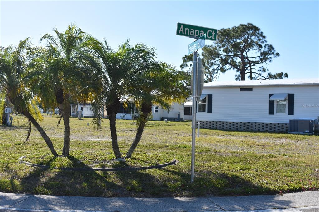 A street sign stands at the corner of a grassy lot with palm trees and houses — 6805 ANAPA COURT, NORTH PORT, FL