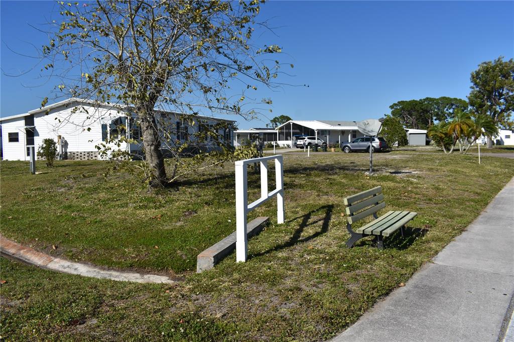 A white mobile home sits behind a grassy yard with a bench and white fence — 6805 ANAPA COURT, NORTH PORT, FL