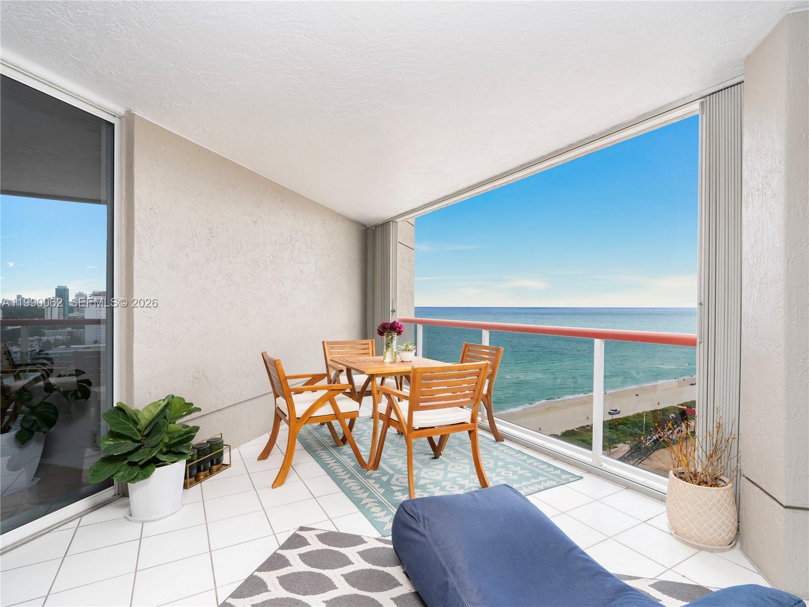 A balcony features a dining set on a patterned rug overlooking the ocean and beach — 6767 Collins Ave # 1704, Miami Beach FL 33141, MIAMI BEACH, FL