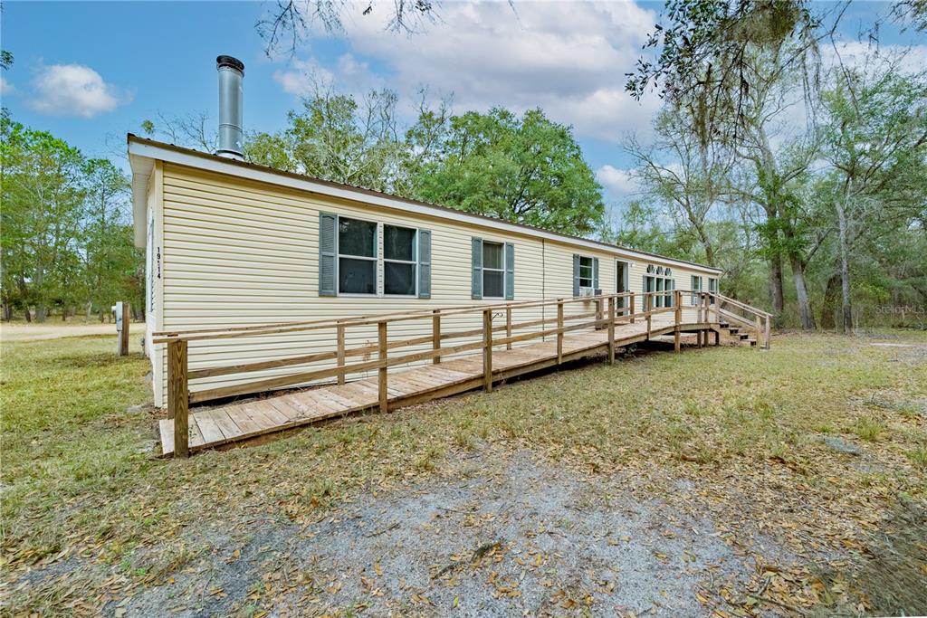 A light yellow manufactured home features a long wooden wheelchair ramp leading to the entrance — 19514 N COUNTY ROAD 225, GAINESVILLE, FL