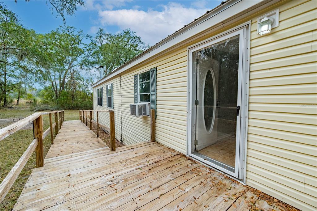 A wooden ramp leads to the side entrance of a yellow-sided mobile home — 19514 N COUNTY ROAD 225, GAINESVILLE, FL