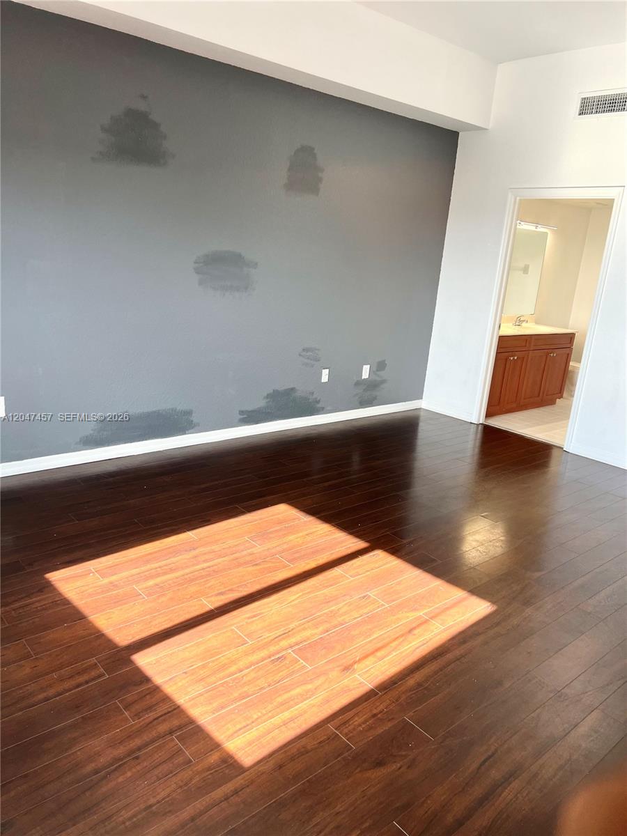 A room with dark wood flooring and a gray accent wall featuring patchy paint — 36 NW 6th Ave # 1, Miami FL 33128, MIAMI, FL