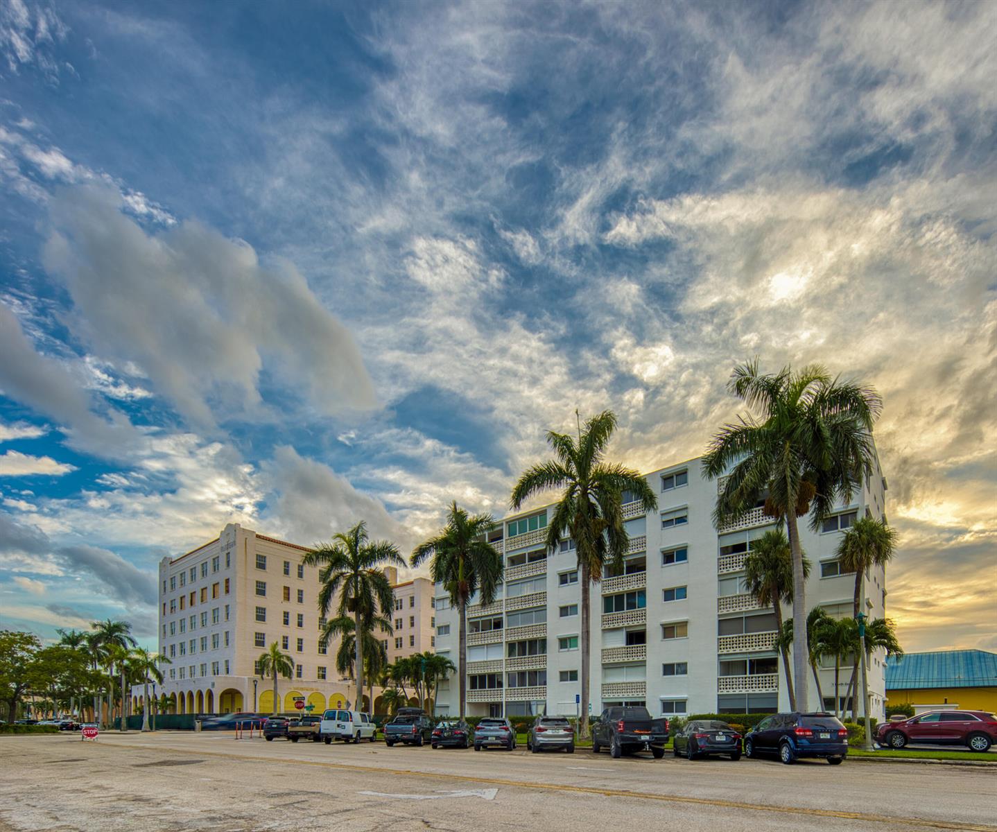 A street-level view of two multi-story apartment buildings lined with palm trees under a cloudy sky — 1 N Golfview Road # 205, FL 33460, FL