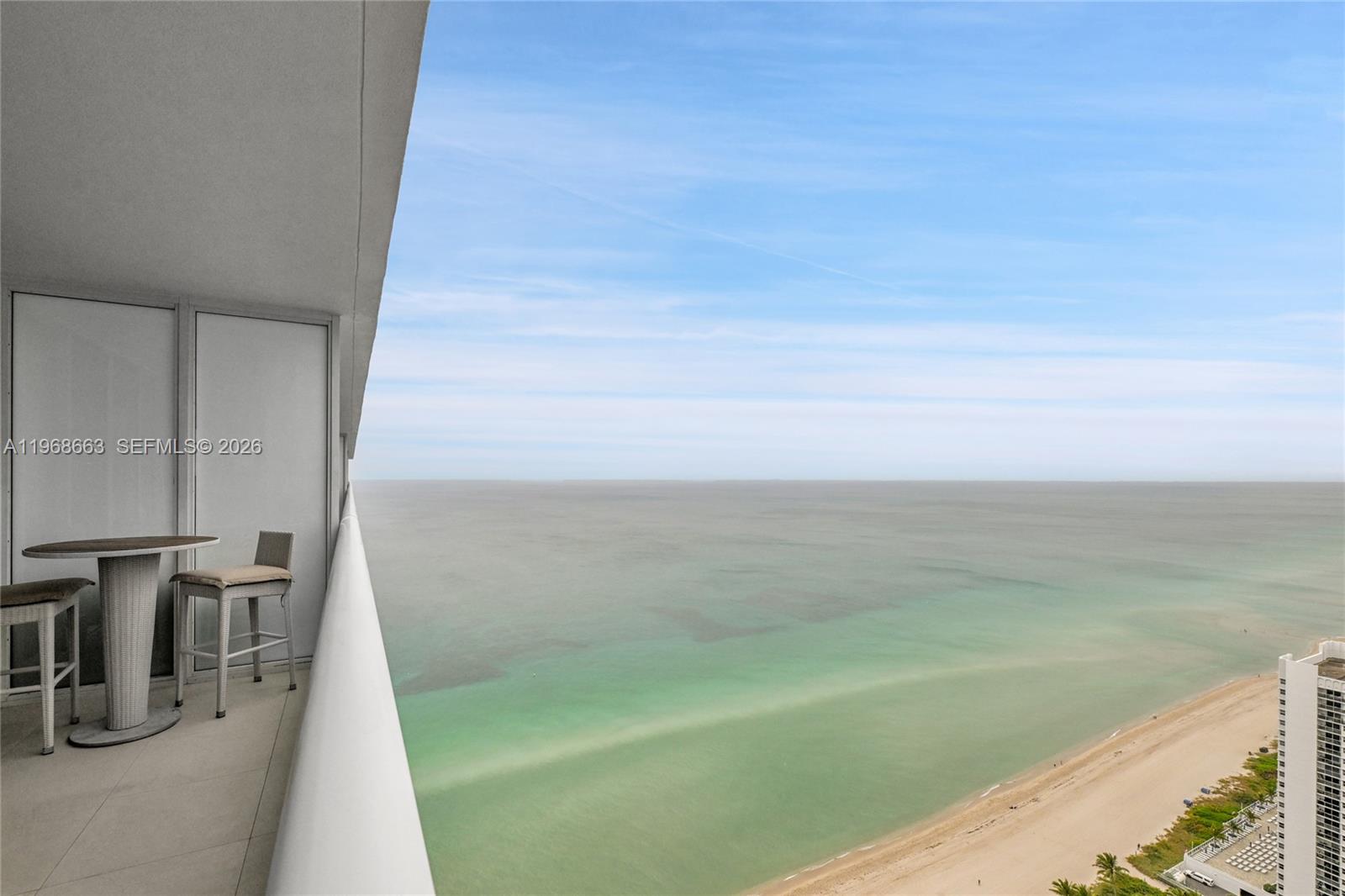 A high-rise balcony features a small table and chairs overlooking the ocean and beach — 1830 S Ocean Dr # 4005, Hallandale Beach FL 33009, HALLANDALE BEACH, FL
