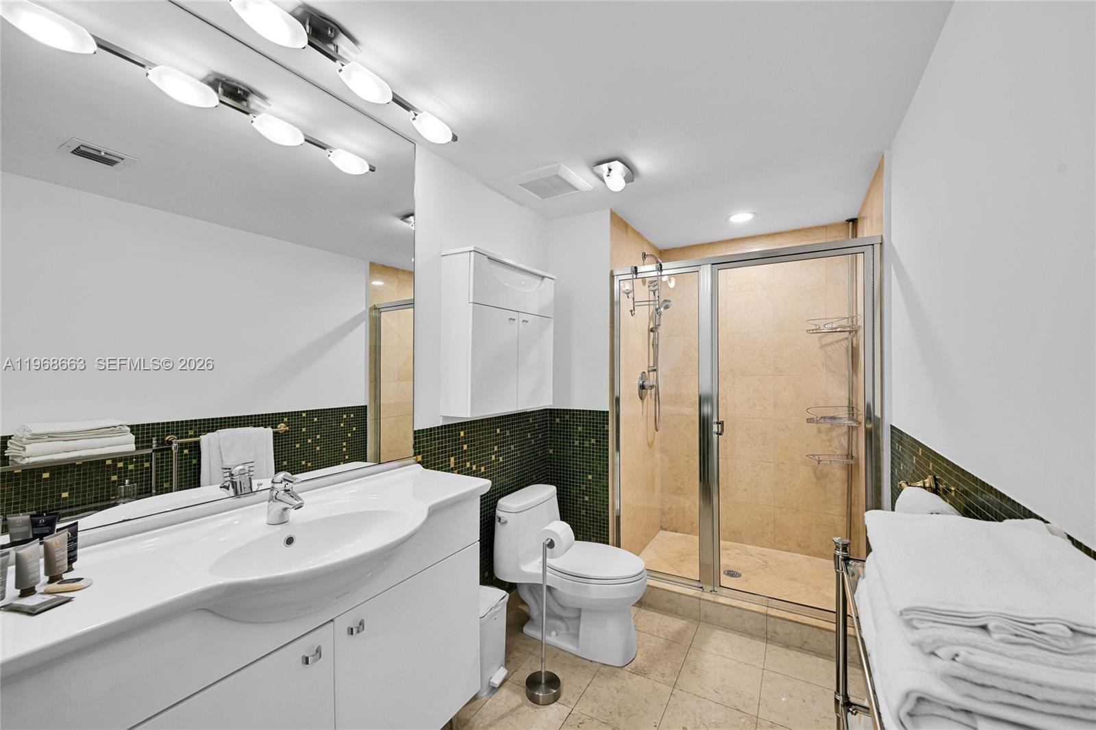 A bathroom features a white vanity, a glass-enclosed shower, and green mosaic tile accents — 1830 S Ocean Dr # 4005, Hallandale Beach FL 33009, HALLANDALE BEACH, FL
