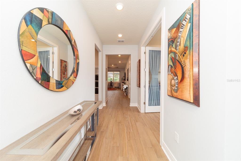 A hallway features light wood-look tile flooring, a round decorative mirror, and abstract wall art — 15139 CANOPY COVER DRIVE, WINTER GARDEN, FL