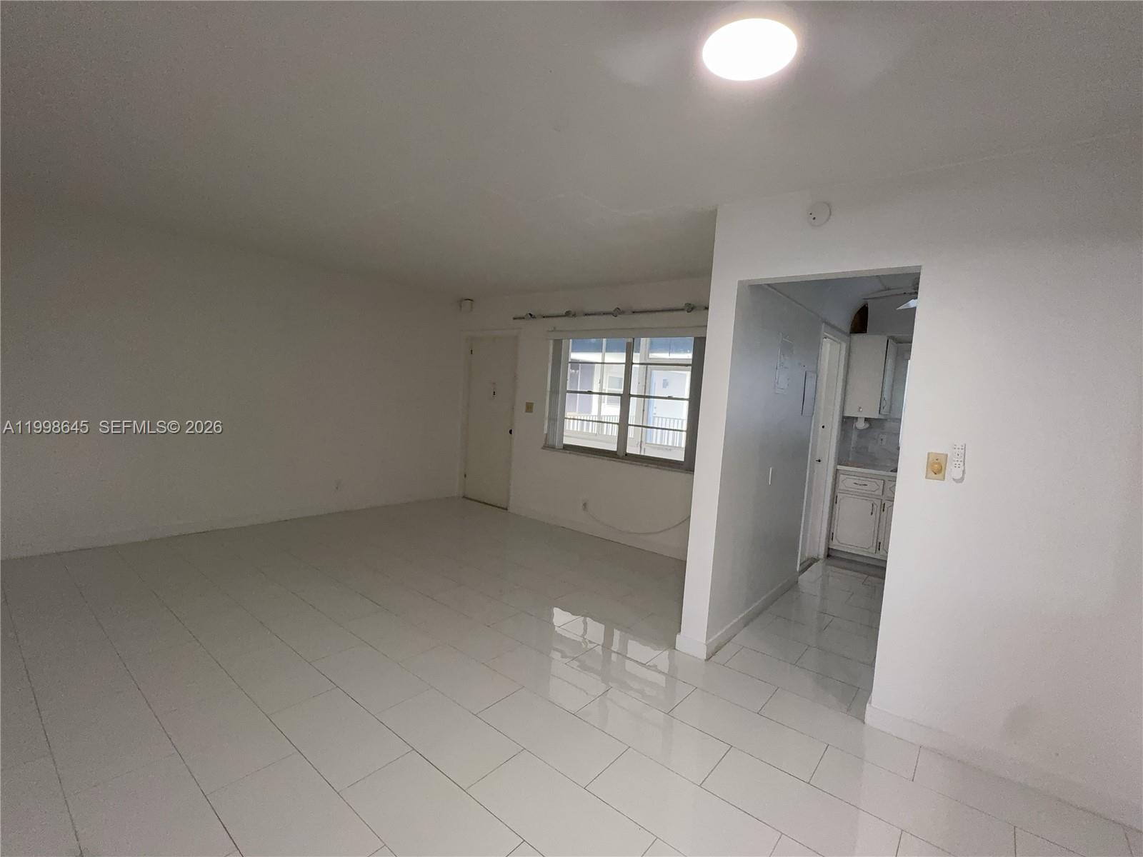 A bright, empty living room features white tile flooring, a window, and an adjacent kitchen — 1943 Monroe St # 306A, Hollywood FL 33020, HOLLYWOOD, FL