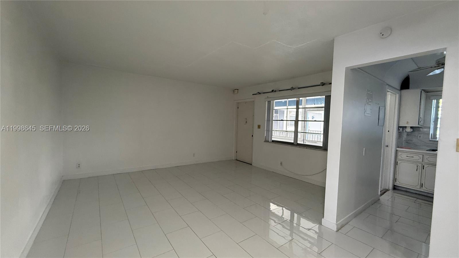 A bright, empty living room features white tile flooring, white walls, and an adjacent kitchen — 1943 Monroe St # 306A, Hollywood FL 33020, HOLLYWOOD, FL