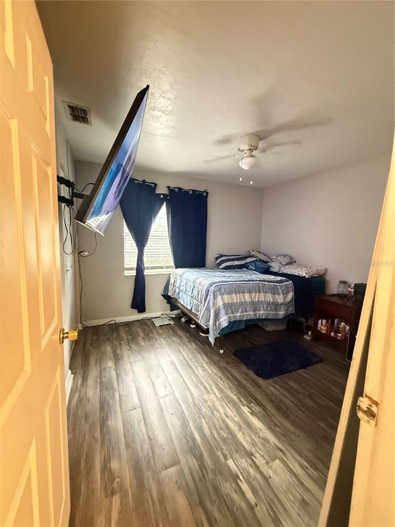 A bedroom features wood-look flooring, a ceiling fan, a wall-mounted television, and a bed — 615 SW 11TH LANE UNIT A, GAINESVILLE, FL