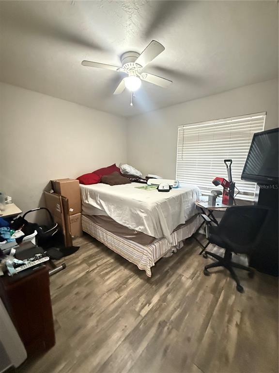 A bedroom features light wood-look flooring, a ceiling fan, and a bed with boxes nearby — 615 SW 11TH LANE UNIT A, GAINESVILLE, FL