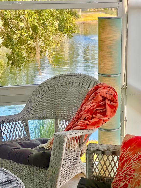 A small bistro table and chairs sit on a tiled sunroom floor overlooking a pond — 7801 ONTARIO STREET CIRCLE, SARASOTA, FL
