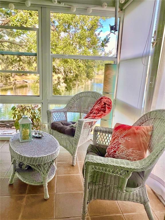 A wicker chair with a coral blanket sits on a sunroom porch overlooking a lake — 7801 ONTARIO STREET CIRCLE, SARASOTA, FL