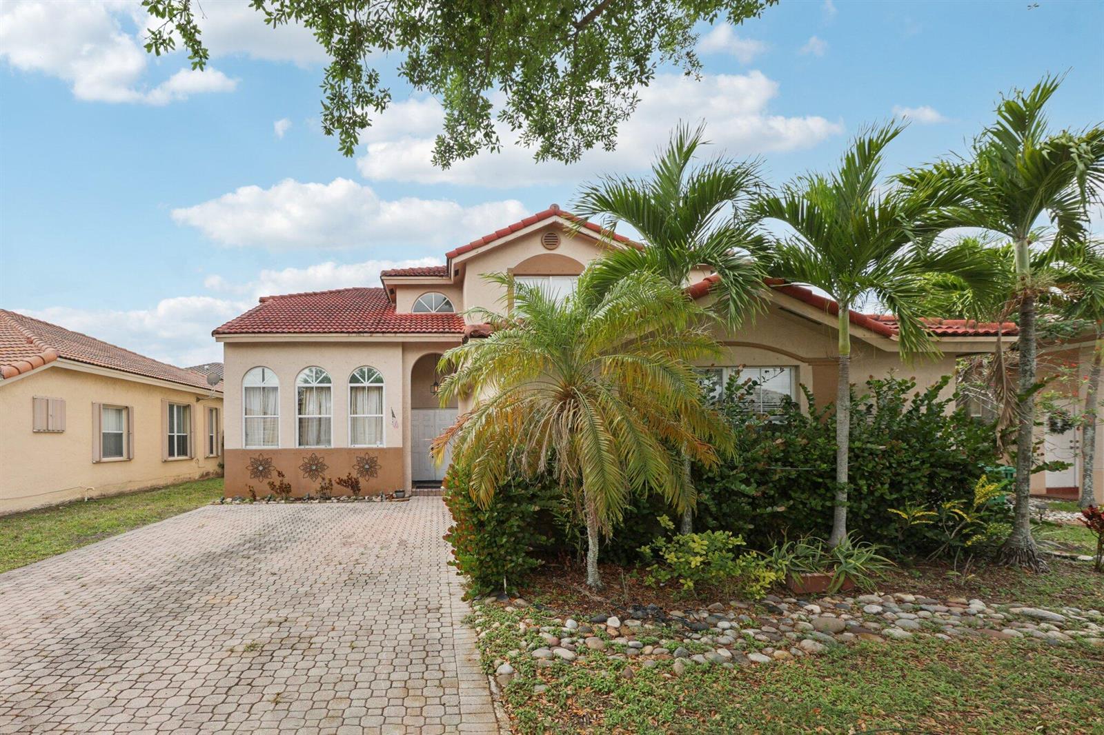 A beige house with a red tile roof and a paved driveway under a blue sky — 405 E Royal Cove Circle, Davie FL 33325, DAVIE, FL