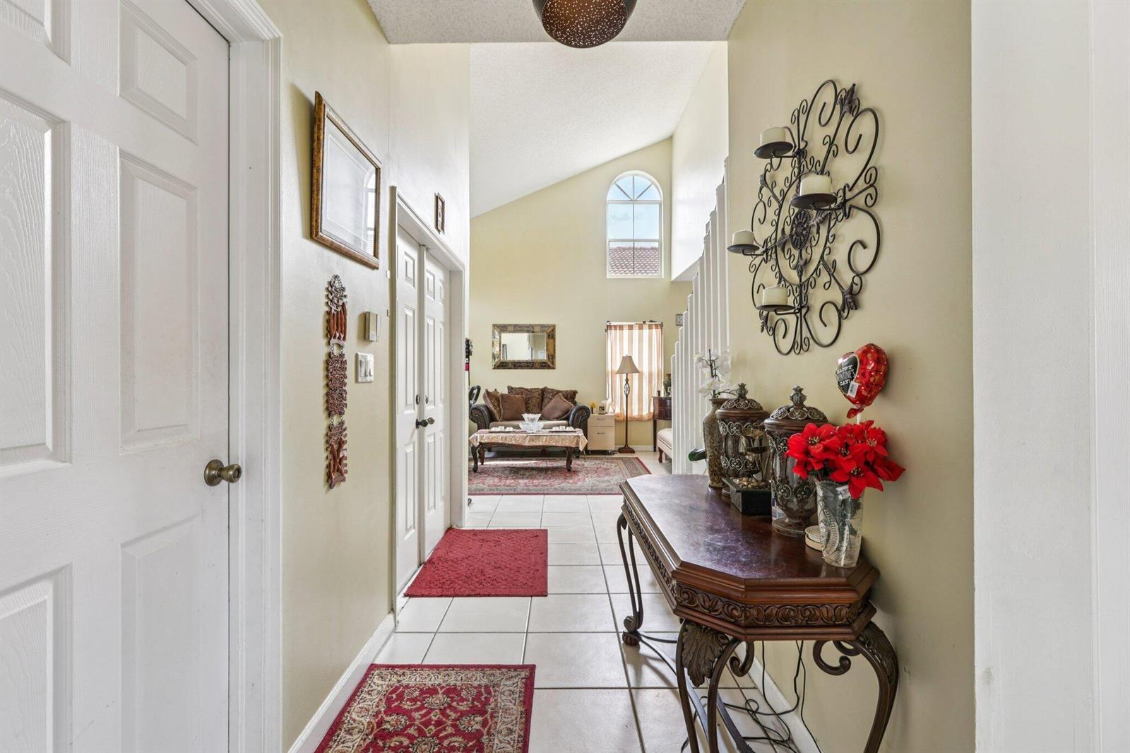A hallway with tile flooring leads to a living room with vaulted ceilings and windows — 405 E Royal Cove Circle, Davie FL 33325, DAVIE, FL