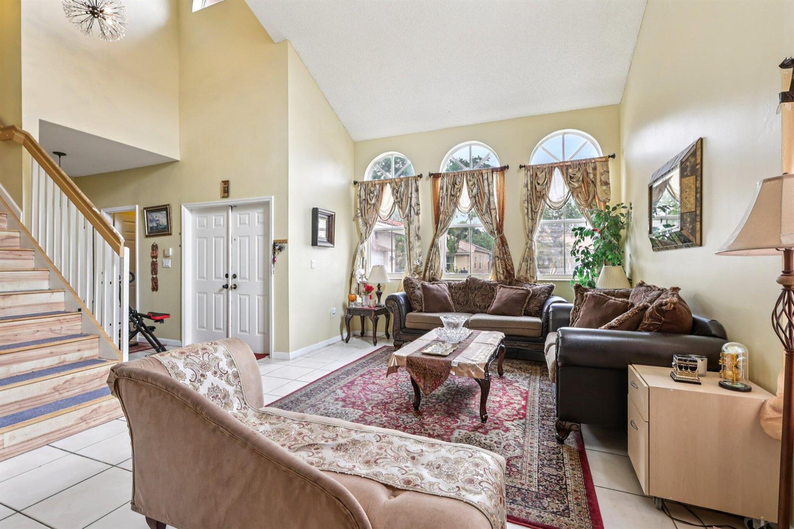A living room features a vaulted ceiling, tiled floors, a staircase, and three arched windows — 405 E Royal Cove Circle, Davie FL 33325, DAVIE, FL