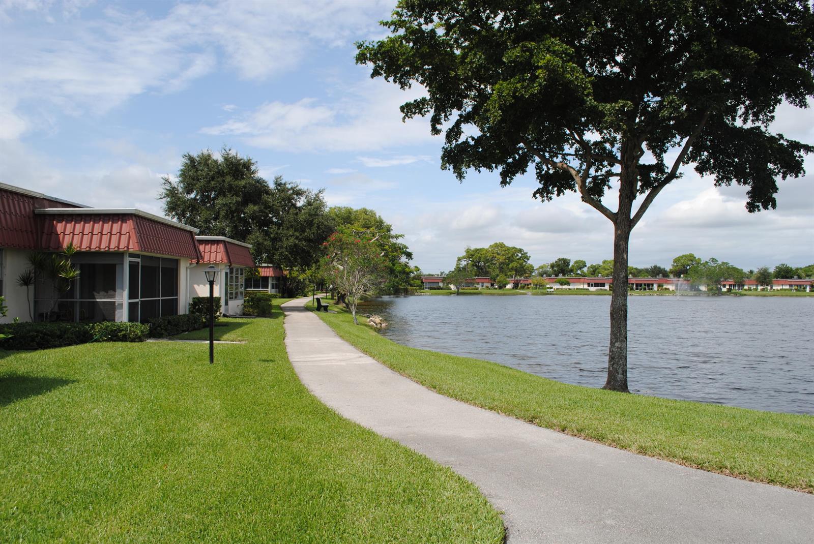 A paved walkway winds along a lake beside residential buildings with red tiled roofs — 815 Salem Lane, Lake Worth FL 33467, LAKE WORTH, FL