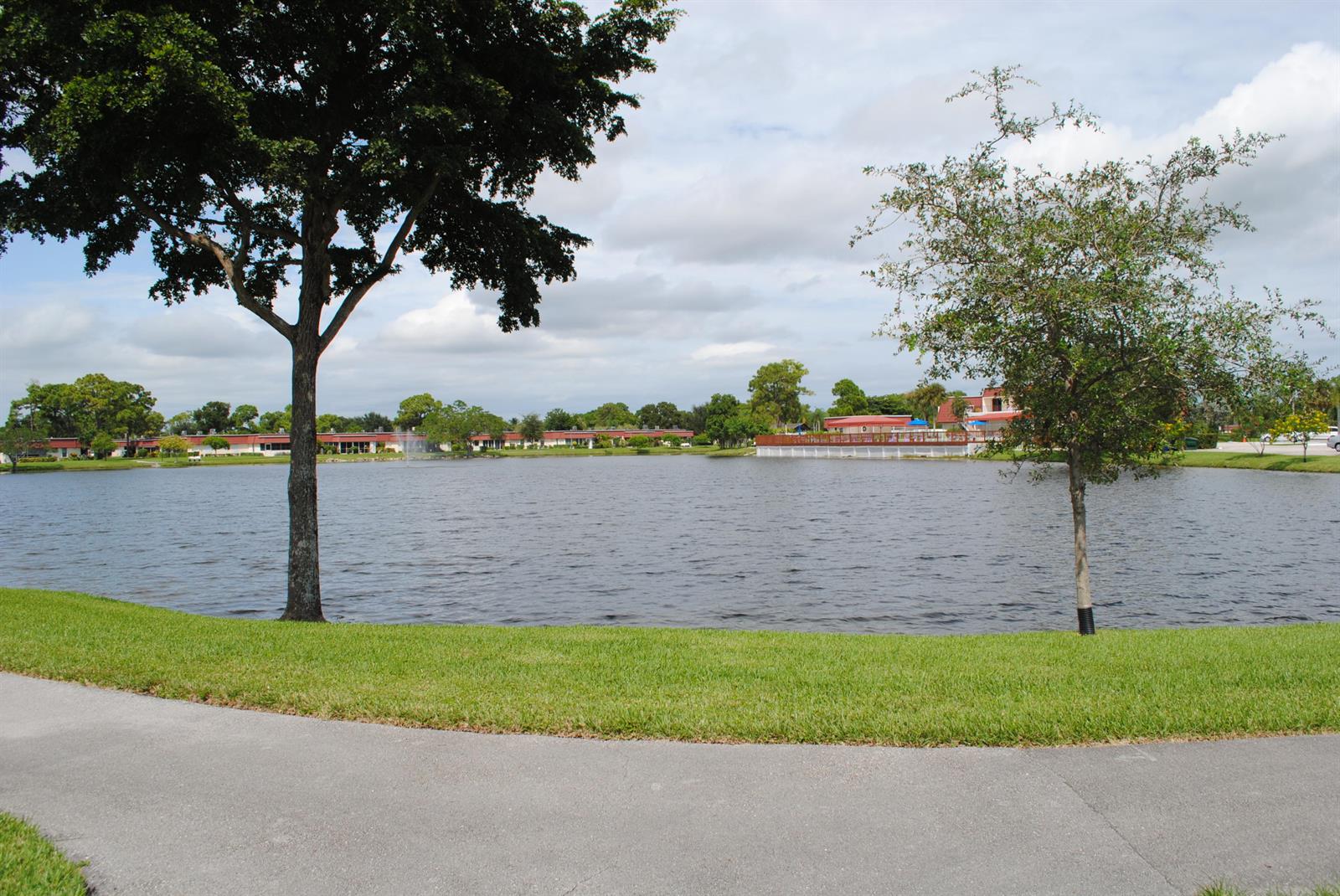 A paved path borders a lake with a fountain and surrounding residential buildings — 815 Salem Lane, Lake Worth FL 33467, LAKE WORTH, FL