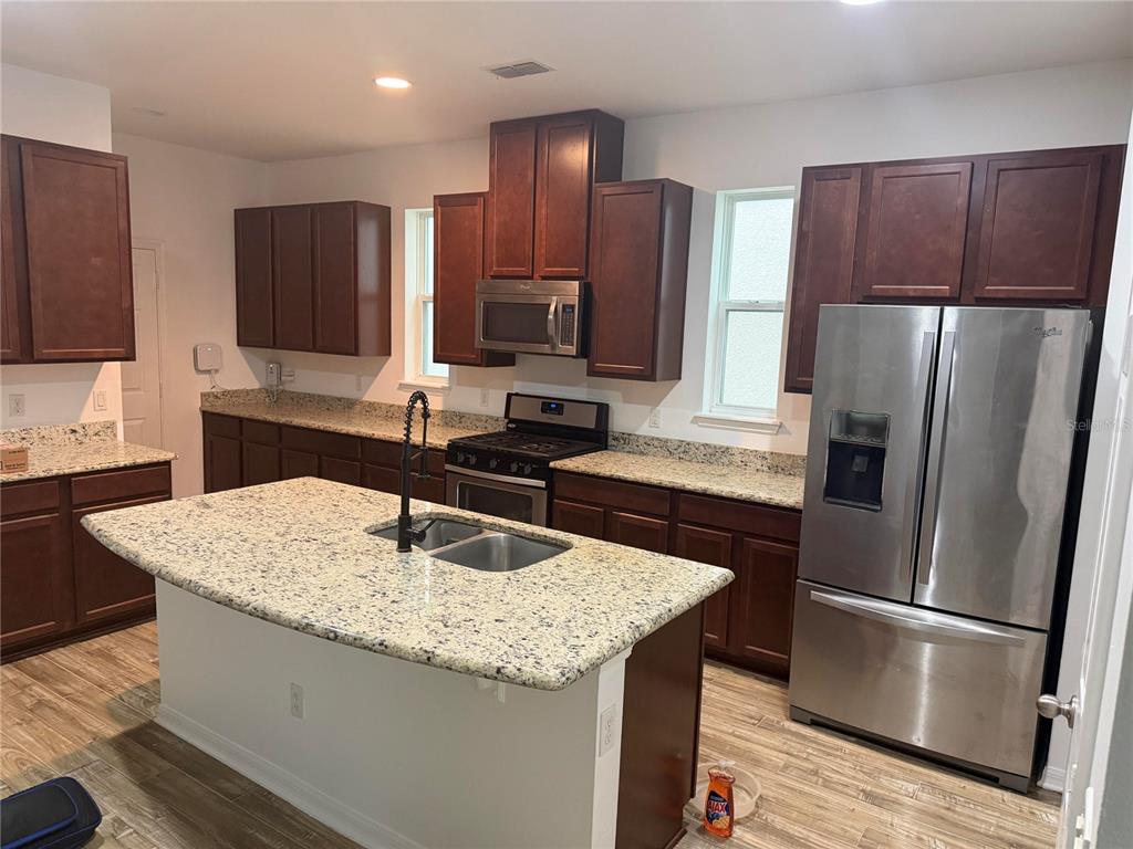 A kitchen features dark wood cabinets, granite countertops, a center island, and stainless steel appliances — 7840 WINTER WREN STREET, WINTER GARDEN, FL