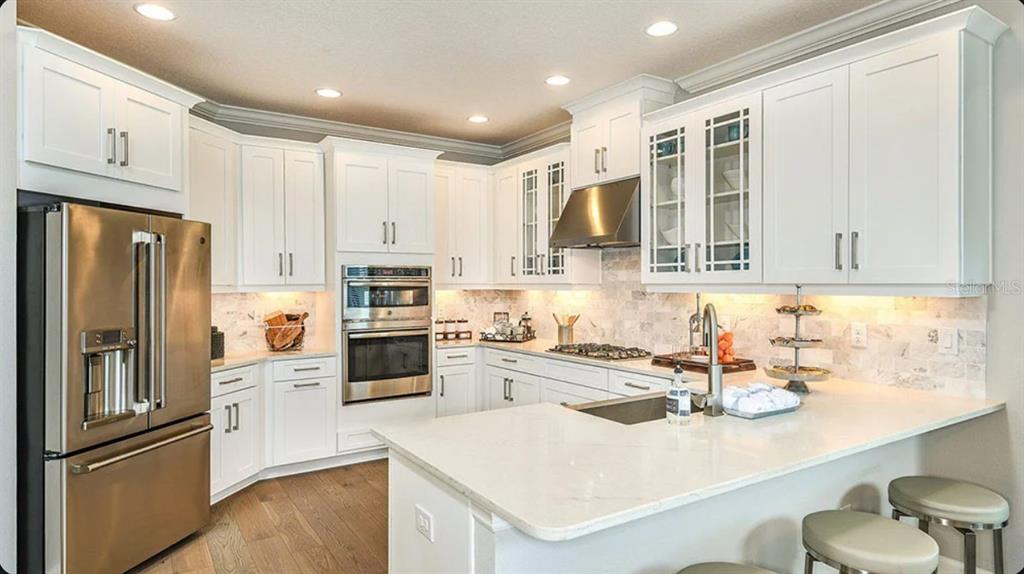 A modern kitchen features white cabinetry, stainless steel appliances, marble backsplash, and a quartz island — 7004 FOXBORO WAY, NOKOMIS, FL