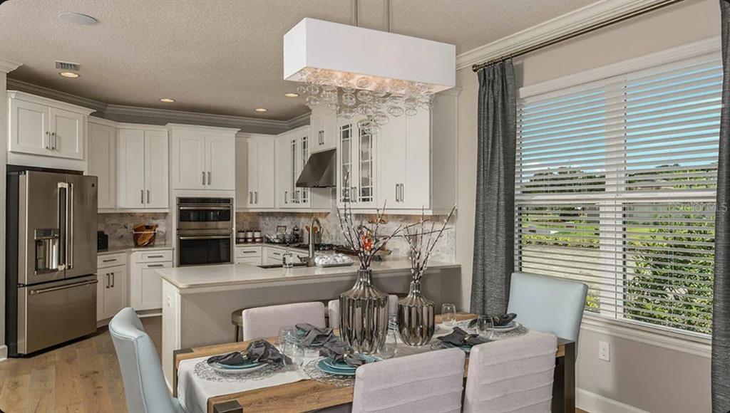 A kitchen with white cabinets and stainless steel appliances overlooks a dining area with seating — 7004 FOXBORO WAY, NOKOMIS, FL