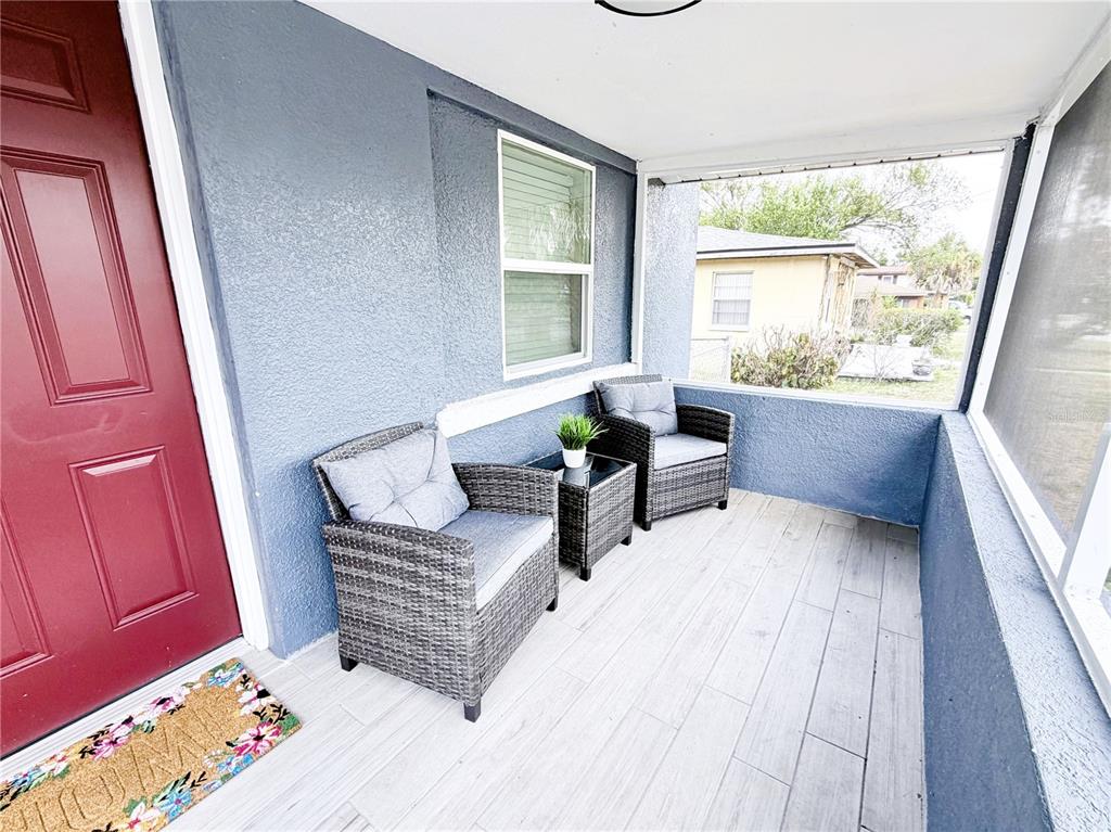 A covered porch features blue stucco walls, light wood-look tile flooring, and two wicker chairs — 1704 MARTIN L KING JR AVENUE, LAKELAND, FL