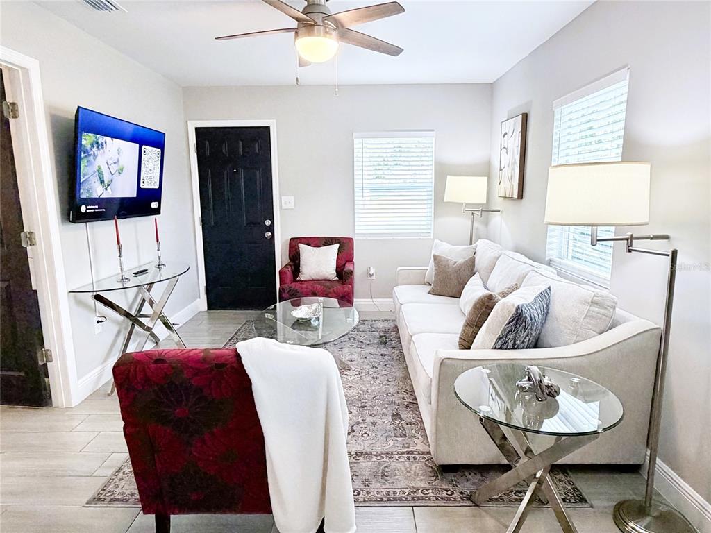 A living room features a white sofa, two patterned armchairs, a glass coffee table, and a television — 1704 MARTIN L KING JR AVENUE, LAKELAND, FL