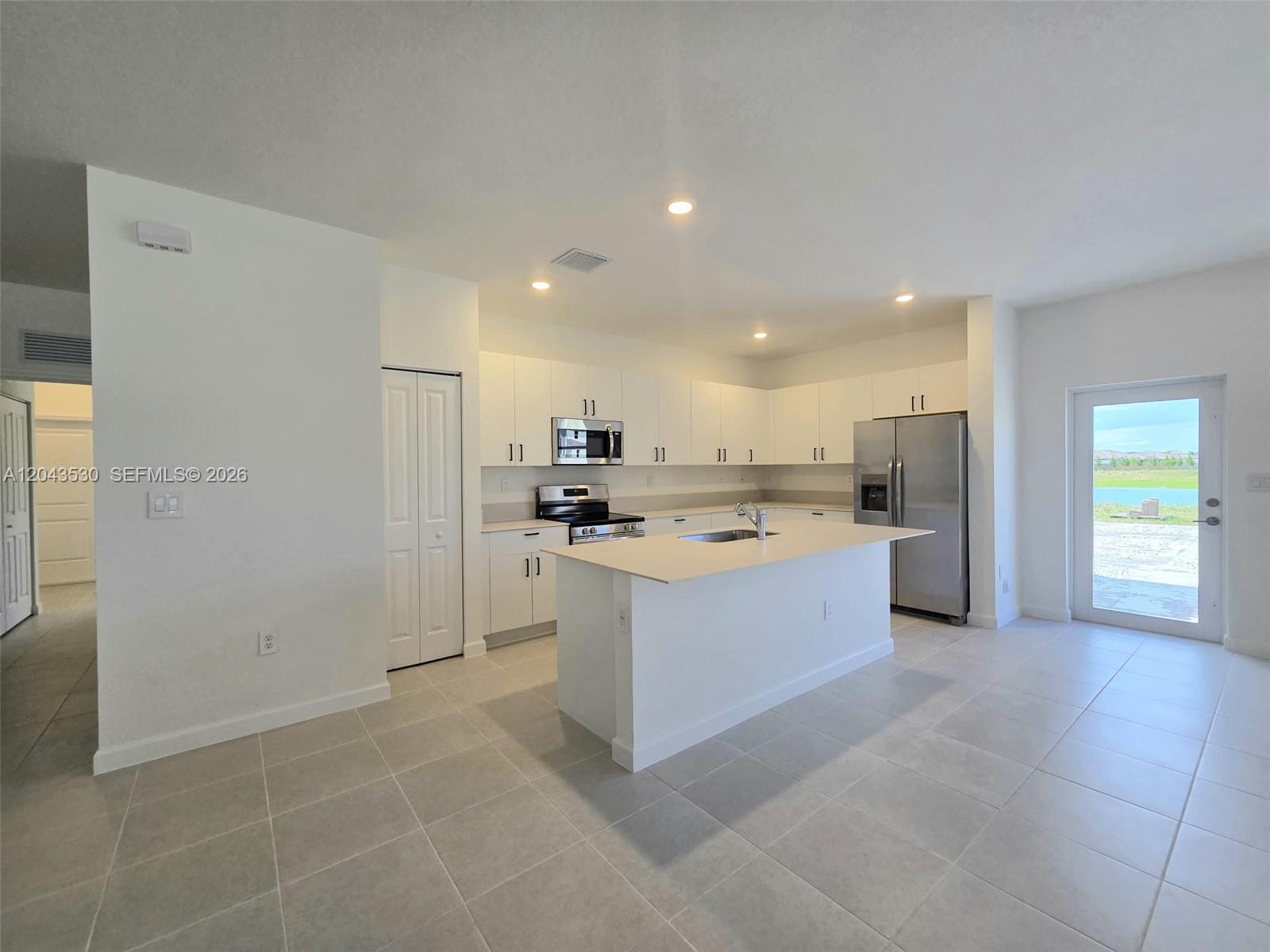 A modern kitchen features white cabinetry, stainless steel appliances, a center island, and tile flooring — 2423 SE 30th St, Homestead FL 33035, HOMESTEAD, FL