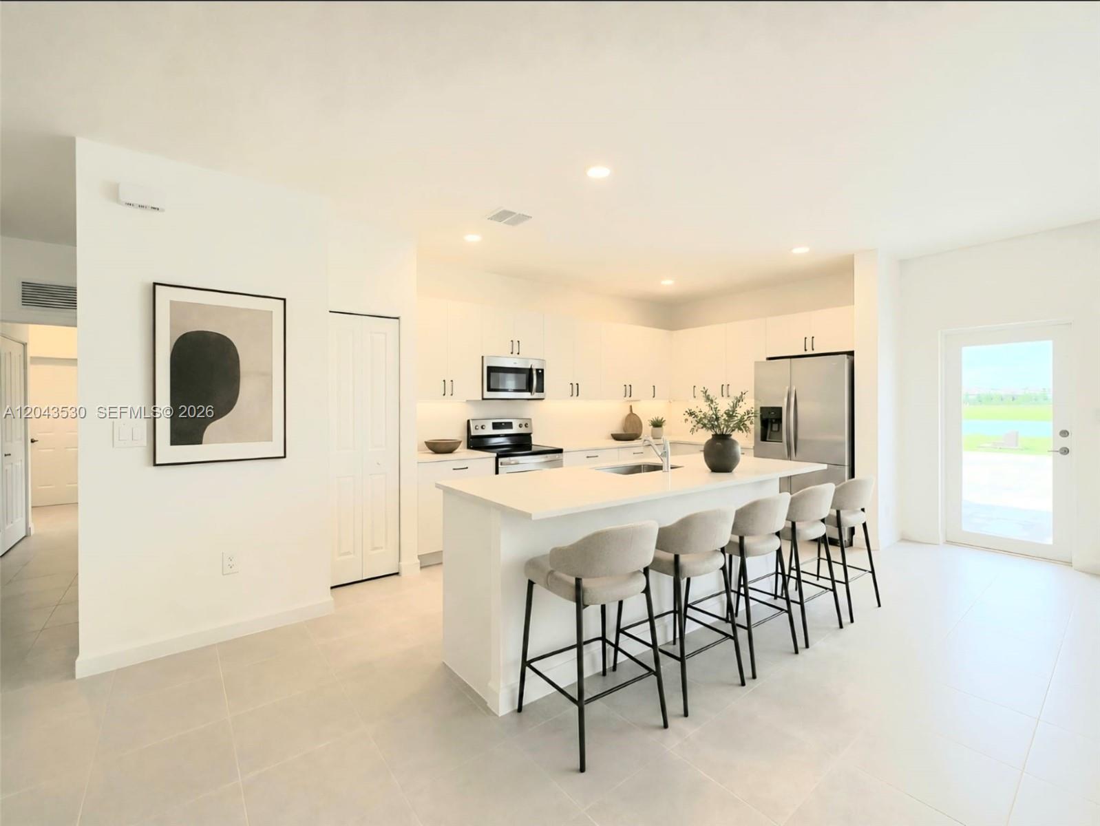 A modern kitchen features white cabinetry, a central island with bar seating, and stainless appliances — 2423 SE 30th St, Homestead FL 33035, HOMESTEAD, FL