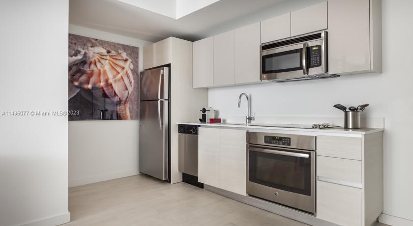 A modern kitchen features light wood cabinets, stainless steel appliances, and a large seashell wall art — 2602 E Hallandale Beach Blvd # R310, Hallandale Beach FL 33009, HALLANDALE BEACH, FL